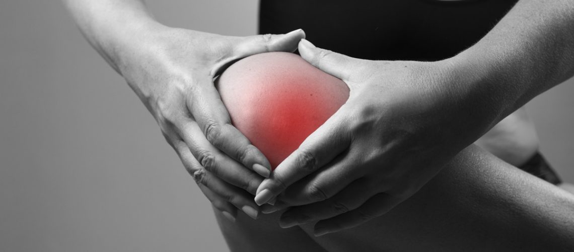 Pain in the knee. Pain in the human body on a gray background. Black and white photo with red dot